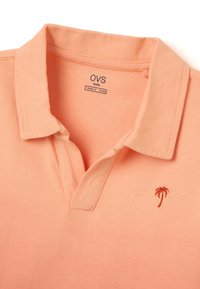Polo para niños de color melocotón con cuello y mangas cortas. Presenta un bordado de una palmera roja en el pecho. Material de algodón suave.