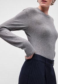 Camisola cinza de mangas compridas feita de material macio, com um design simples. Combinada com calças azul marinho com riscas, apresentando uma silhueta ajustada.