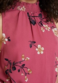 Krátký rukáv blůzka z růžové látky, s nařaseným výstřihem a květinovými vzory v béžové a černé barvě, s hladkou textrurou.