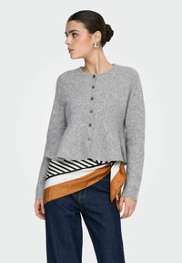 Sivi vuneni kardigan s okruglim izrezom, zatvaranjem sprijeda na kopčanje i proširenim rubom. Uparen s prugastim i jednobojnim šalovima.