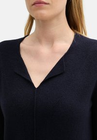 Marineblauer Strickpullover mit V-Ausschnitt, der über einen strukturierten Stoff, dezente Akzente an den Schulternähten und eine taillierte Silhouette verfügt.