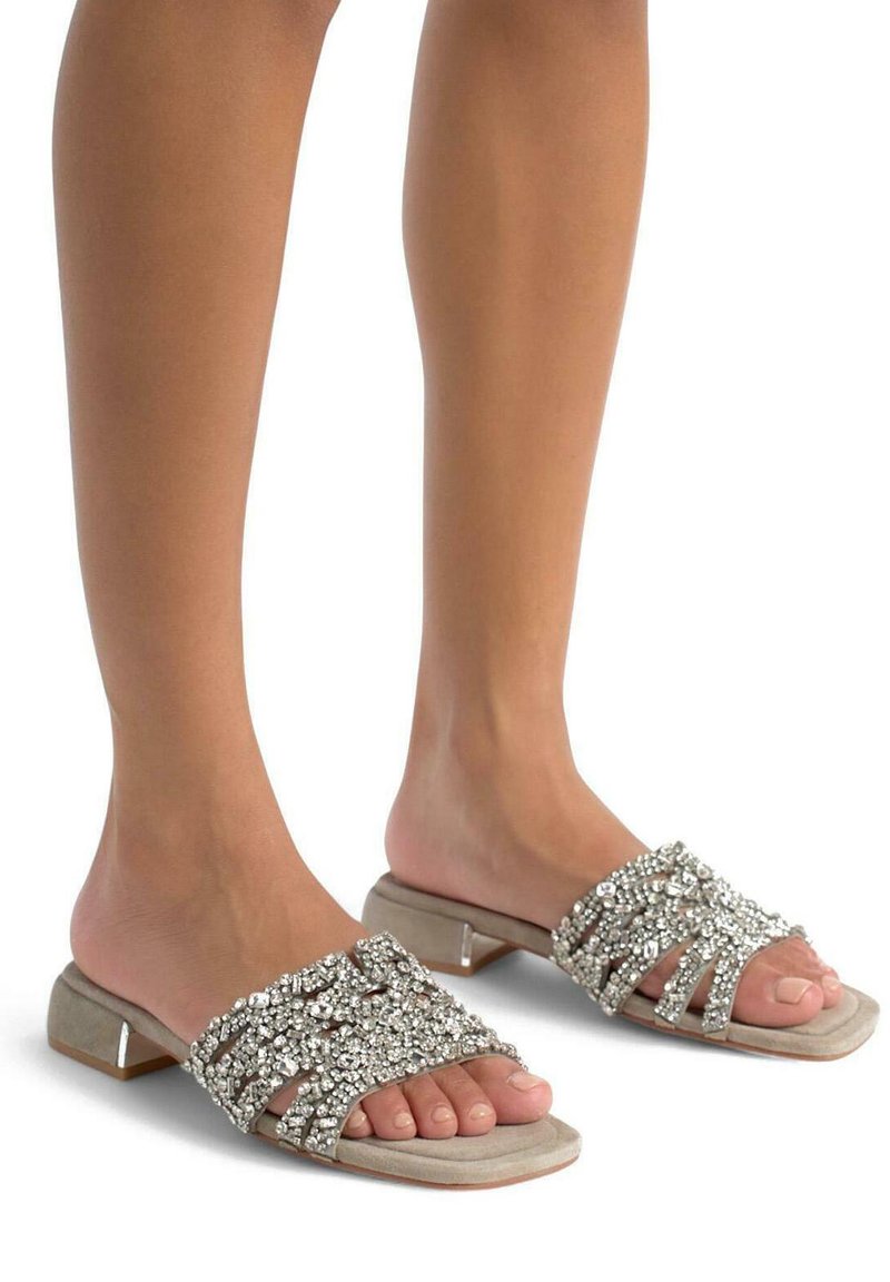 Beige instapsandalen met een gestructureerde, glinsterende bovenkant versierd met strass-steentjes. De hak is laag en blokvormig, wat zorgt voor stabiliteit.