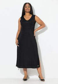 Mustaton olkaimeton mekko V-pääntiellä, virtaavalla siluetilla, sivuhalkiolla ja hillitty kultainen yksityiskohta helmassa. Tasainen kankaan pinta.