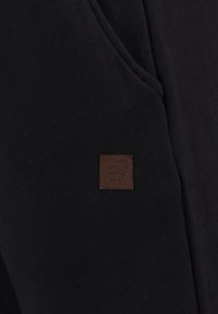 Zwarte stof met een gladde textuur, voorzien van een klein bruin leren label met de opdruk "KEY LARGO" en een logo ontwerp.
