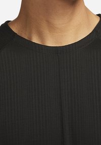 Zwarte geribde stof, close-up van een overhemdkraag en schouderdetails met een gladde textuur en subtiele stikaccenten.