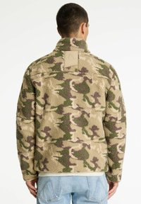 Fleecejack in beige camouflage met groene en bruine patronen. Voorzien van een hoge kraag en een patch op de bovenrug. Zachte textuur.