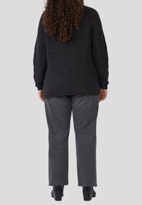 Dunkler Strickpullover mit lässiger Passform, langen Ärmeln und geripptem Muster, kombiniert mit grauen Jeans mit ausgefransten Säumen und schwarzen Ankle Boots.