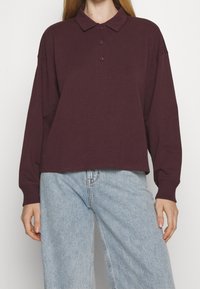 Burgundská dlouhý rukáv polokošile s límečkem, s knoflíkovou légou vpředu a žebrovanými manžetami, doplněná světle modrými džínami.