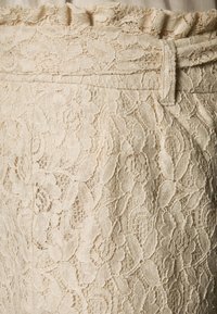 Lace shorts i krämfärg med ett texturerat blommönster. Har en fransad midja och en bältesslinga, vilket framhäver de intrikata detaljerna genom hela plagget.