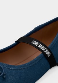 Μπλε υφασμάτινη επίπεδη γόβα με μαύρη ελαστική λωρίδα στο πάνω μέρος, τυπωμένη με τη φράση "LOVE MOSCHINO" με λευκά γράμματα.