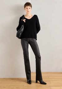 Černý pletený svetr s výstřihem do V, nosí se s černými přiléhavými kalhotami z imitace kůže a lodičkami s špičatou špičkou. Modelka nese skládací černou tašku.