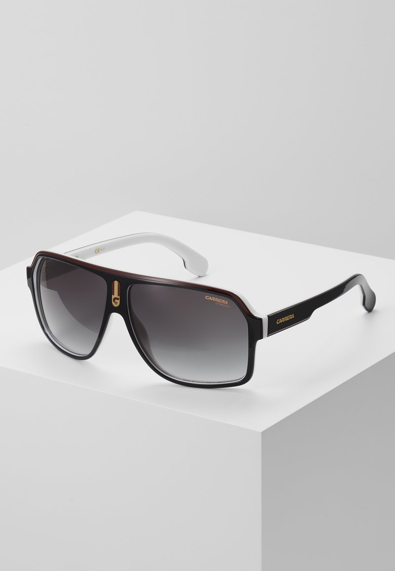 Sunglasses with a brown and black plastic frame, grey gradient lenses, white arms, and gold logo detailing on the front and side.