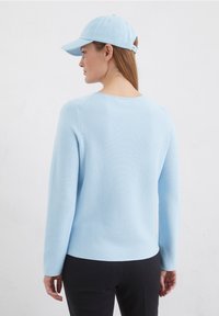 Helles blaues Strickpullover mit langen Ärmeln und rundem Ausschnitt, kombiniert mit einer passenden Mütze. Glatte Textur, minimale Designmerkmale.