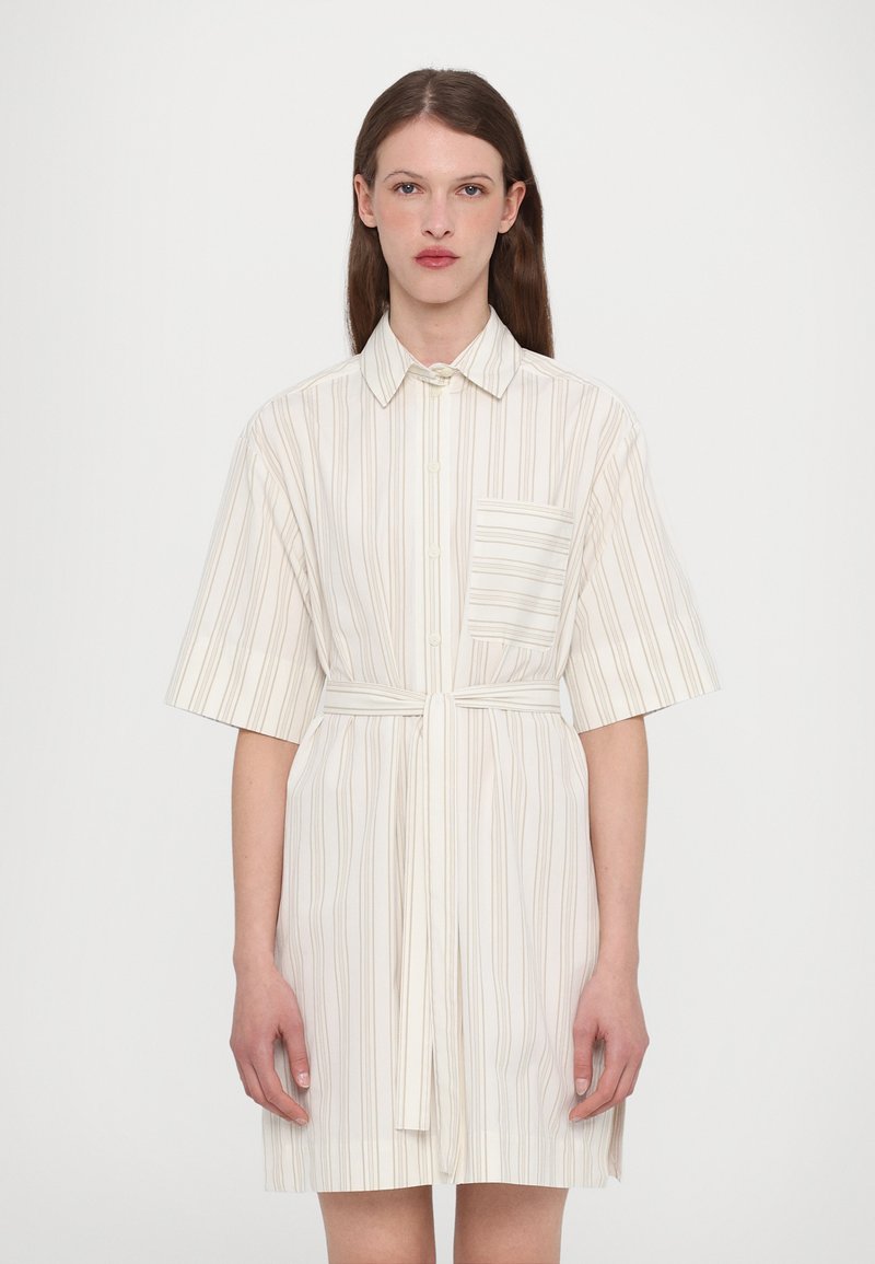 Abito camicia a maniche corte, colore crema chiaro, con righe verticali color beige, chiusura frontale a bottoni e una cintura da annodare in vita. Presenta una tasca sul petto.