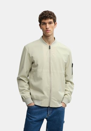 Bomber jacket beige chiaro con zip frontale, polsini a coste e tasca laterale. Presenta una texture morbida e un design minimalista.