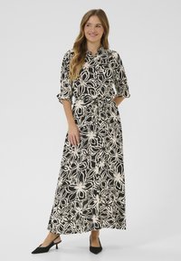 Robe maxi noire avec un motif floral blanc, présentant un devant à boutons, des manches courtes repliées et un détail de taille nouée.