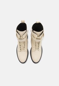 Beige lær ankle boots med sorte såler, med snørebånd, detalj med rem og glidelås bak. Glatt tekstur.
