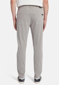 Pantalons en coton gris à coupe droite, poches arrière visibles et boucle à la taille. Portés avec des baskets sombres.