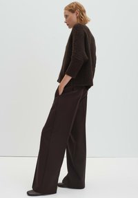 Maglione marrone con trama, spalle scese, abbinato a pantaloni a vita alta, gamba larga, di colore marrone scuro. Scarpe in pelle liscia completano l'outfit.