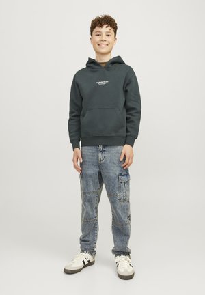 Felpa con cappuccio verde scuro dotata di tasca a marsupio, abbinata a jeans cargo azzurri chiari con più tasche e una vestibilità comoda. Sneakers bianche.