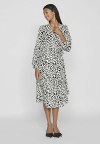 Črno-bele vzorčaste obleke z dolgimi napihnjenimi rokavi, ki segajo do sredine meč, v kombinaciji s črnimi čevlji z mašnjo. Gladka tekstura tkanine.