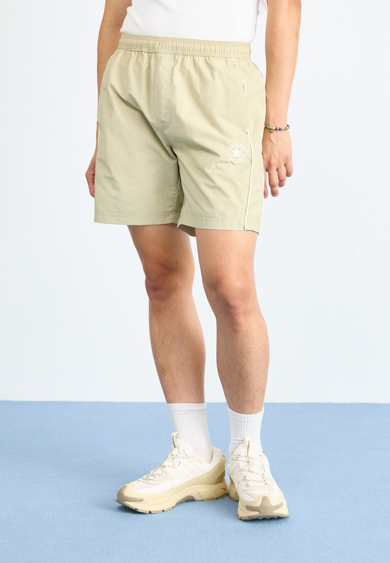 Lysegrønne shorts med elastisk midje, sidelister og trykt logo på venstre ben. Brukt med hvite sokker og beige joggesko.