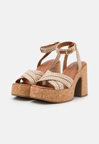 Beige braided sandals with cork platform heels. Features adjustable ankle straps and a soft brown insole for comfort.