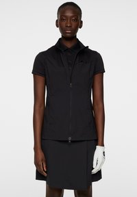 Svart golfväst med krage och korta ärmar, med en central dragkedja och sidofickor. Bärs med en svart kjol och vit handske.