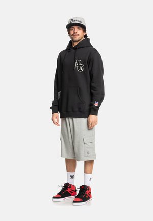 Sudadera negra con logo, pantalones cortos cargo grises y zapatillas negras/rojas. Diseño casual, con bolsillo frontal y calcetines a rayas. Gorra gris con logo.