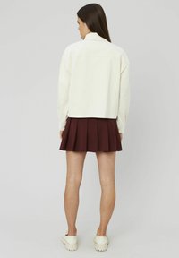 Veste en velours côtelé ivoire avec un col, des épaules dénudées et un fond court, associée à une mini-jupe plissée bordeaux et des chaussures à plateforme blanches.