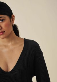 Maglione a costine nere con scollatura a V profonda e maniche lunghe, che mette in risalto un tessuto testurizzato su uno sfondo neutro.