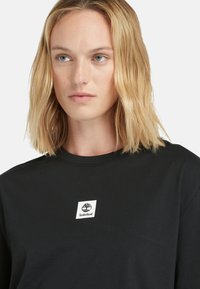 Schwarz Baumwoll-T-Shirt mit Rundhalsausschnitt und kurzen Ärmeln, versehen mit einem weißen quadratischen Logo-Patch mit einem Baumgrafik und dem Text "Timberland".