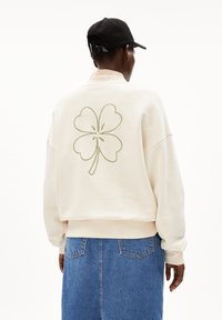 Crème-kleurige sweatshirt met een groot groen geborduurd klavertje vier op de achterkant. Gecombineerd met een blauwe denimrok.