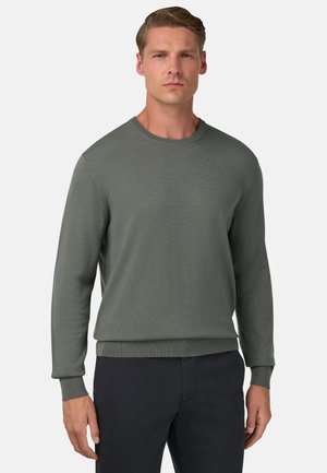 Grauer Strickpullover mit rundem Halsausschnitt und gerippten Bündchen und Saum; glatte Textur. Kombiniert mit dunklen Hosen, getragen von einem männlichen Model.
