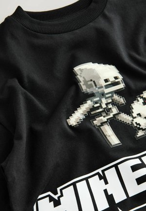 Fekete pamut pulóver, amelyen fehér és szürke színű pixeles játékkarakterek láthatók, alatta vastag "MINECRAFT" felirattal. Puha textúrájú.