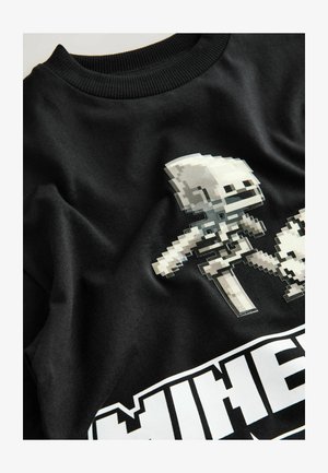 Zwart katoenen sweatshirt met gepixelde spelpersonages in wit en grijs gedrukt, met daaronder de gedurfde tekst "MINECRAFT". Zachte textuur.