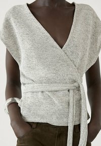 Light gray wrap top with a deep V-neck, short sleeves, and a tie at the waist, made from soft knit fabric.