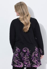 Tunique noire à manches longues ornée de motifs floraux violets au bas et aux manches, fabriquée dans un tissu doux à la texture lisse.
