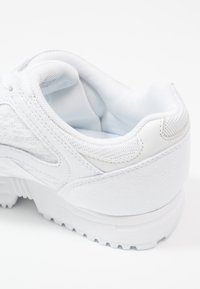 Vit träningsskor med en texturerad mesh-överdela och släta läderdetaljer. Har en vadderad krage och en solid gummisula med bra grepp.