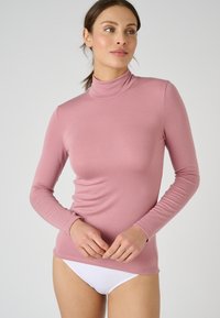 Maglietta a manica lunga color rosa chiaro con collo a nanoruota, texture a coste, design attillato e finitura liscia. Abbinata a biancheria intima bianca.