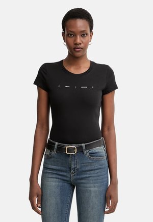 Donna che indossa una maglietta nera aderente Armani Exchange con logo bianco, jeans blu e cintura nera con fibbia dorata.