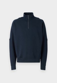 Marine blå hettegenser med glidelås, høy krage, ribbestrikkede mansjetter og en myk tekstur. Subtil merking på brystet. Klassisk, uformell design.