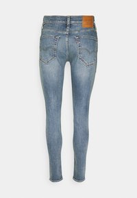 Jean skinny bleu clair avec poches arrière, surpiqûres contrastantes, passants de ceinture et une étiquette de marque en cuir marron sur la ceinture.