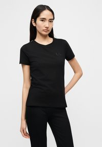 Μαύρο βαμβακερό μπλουζάκι με στρογγυλή λαιμόκοψη και κοντά μανίκια. Διαθέτει διακριτικό λογότυπο στο στήθος και εφαρμοστή γραμμή. Ομαλή υφή.