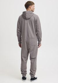 Grey hooded jumpsuit with a back pocket, ribbed cuffs, and elastic hems. Soft fabric and relaxed fit suitable for casual wear.