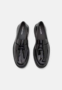 Schwarze Lackleder-Loafers mit einer glatten, glänzenden Oberfläche, die ein genähtes Band über der Oberseite und eine dicke Gummisohle aufweisen.
