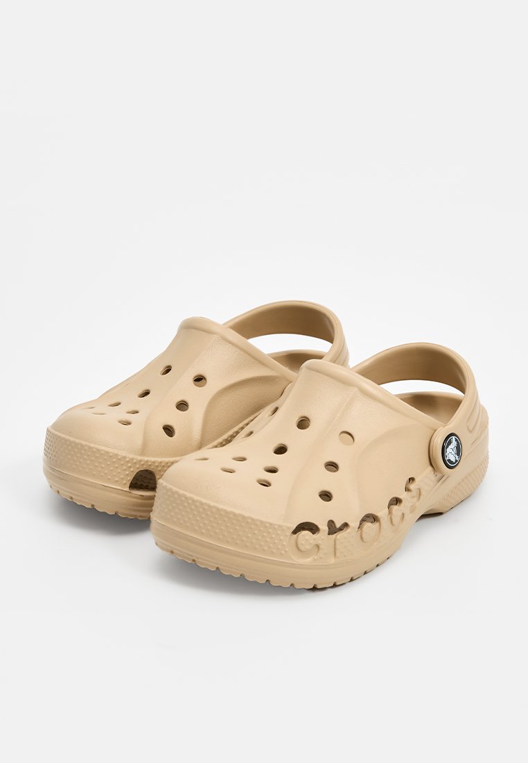Beige Crocs klompen gemaakt van lichtgewicht materiaal, met grote ventilatiegaten, een achterband en het kenmerkende logo aan de zijkant.