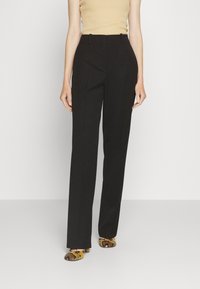 Pantalon noir sur mesure à coupe droite, en tissu lisse, avec passants pour ceinture et poches latérales, accompagné de chaussures à talons à motifs.
