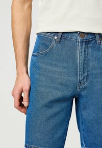 Spijkerbroek shorts in een medium blauwe wassing met een rechte snit, voorzien van een knoop- en ritssluiting, voorzakken en een lichte vervaging.