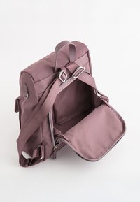 Lila Stoff-Rucksack mit rechteckiger Form, ausgestattet mit einem Reißverschluss, verstellbaren Trägern und einer vorderen Klappe. Glatte Textur, minimale Hardware.